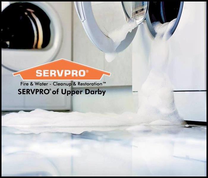 Sudsy water pouring out of a front loading washing machine onto white tile floor