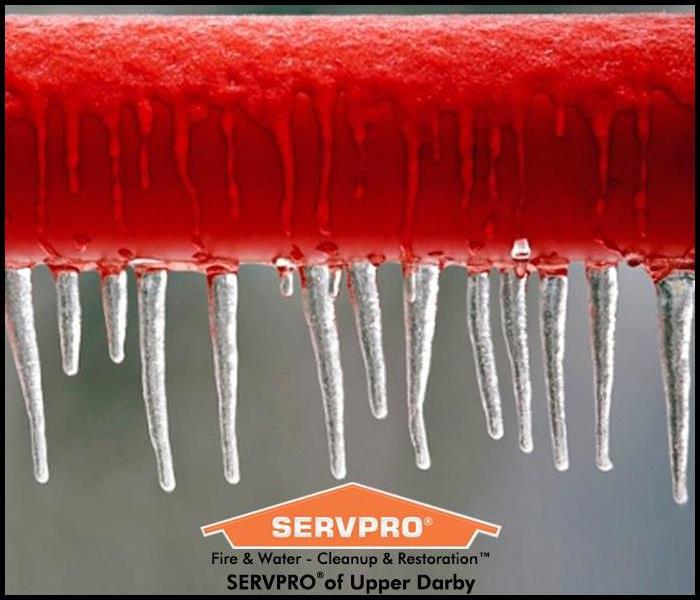 Close up of a red pipe with frozen icicles hanging off of it and the SERVPRO logo